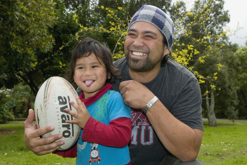 A happy child playing with a rugby ball being embraced from behind by a male parent figure